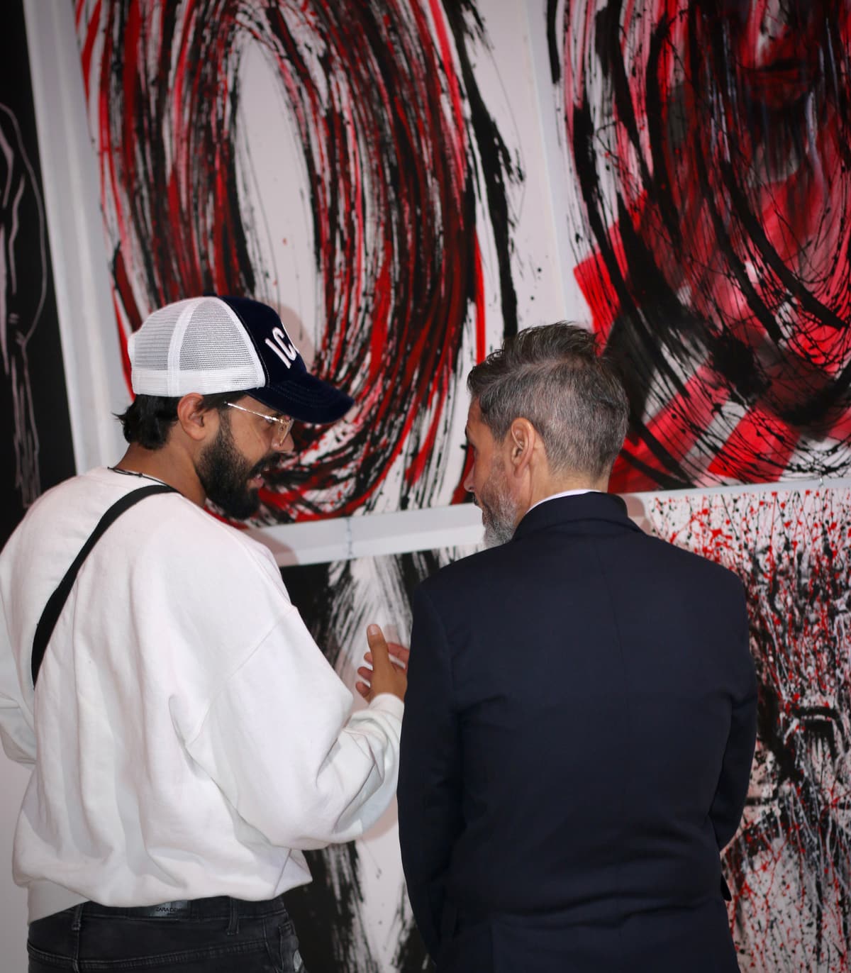 Kamal Hannouda in conversation with another man in front of a large red, black, and white abstract painting.