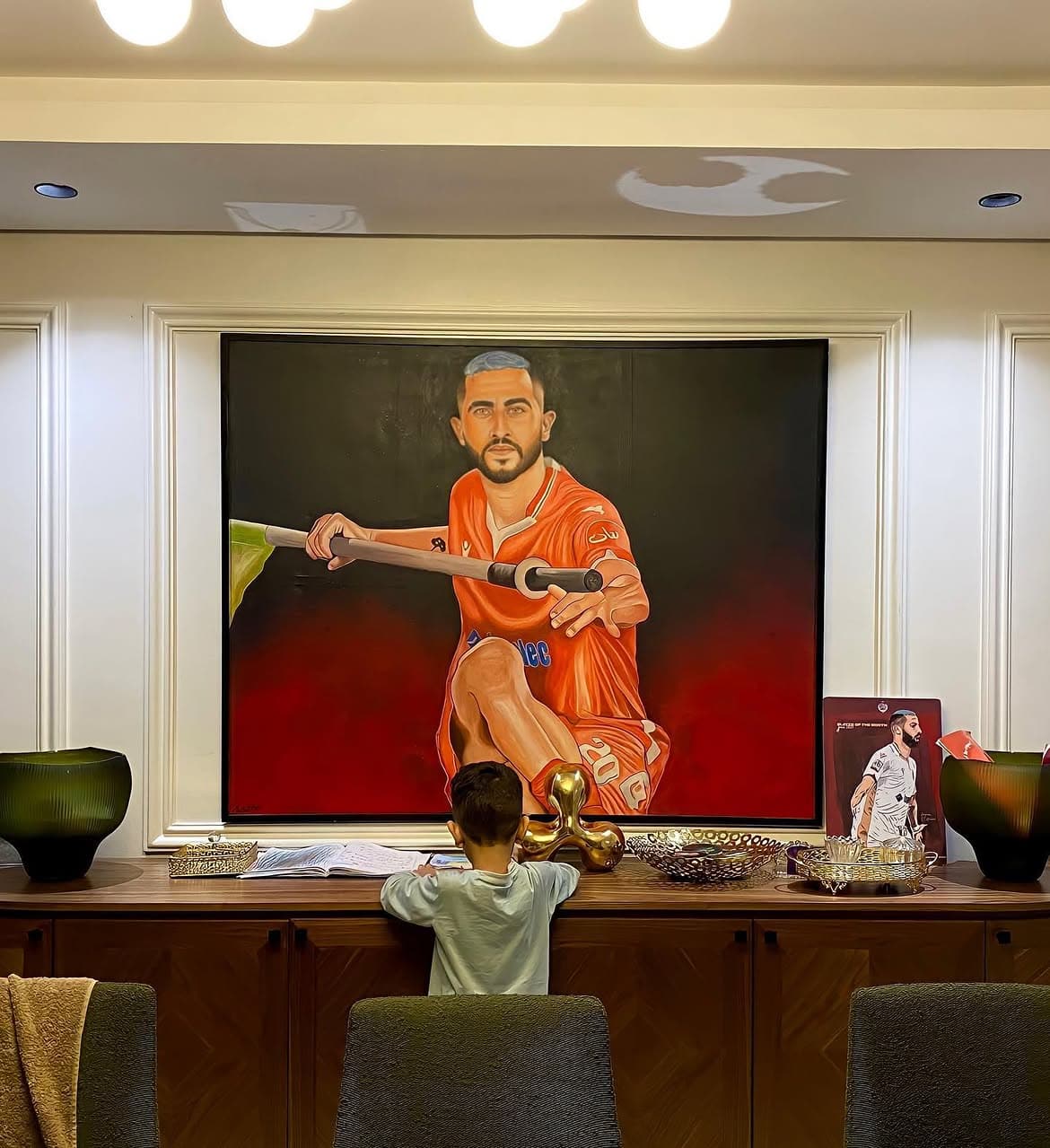 Framed portrait painting of Aymane El Hassouni in Wydad Athletic Club's red-and-white kit, displayed on a wooden sideboard.