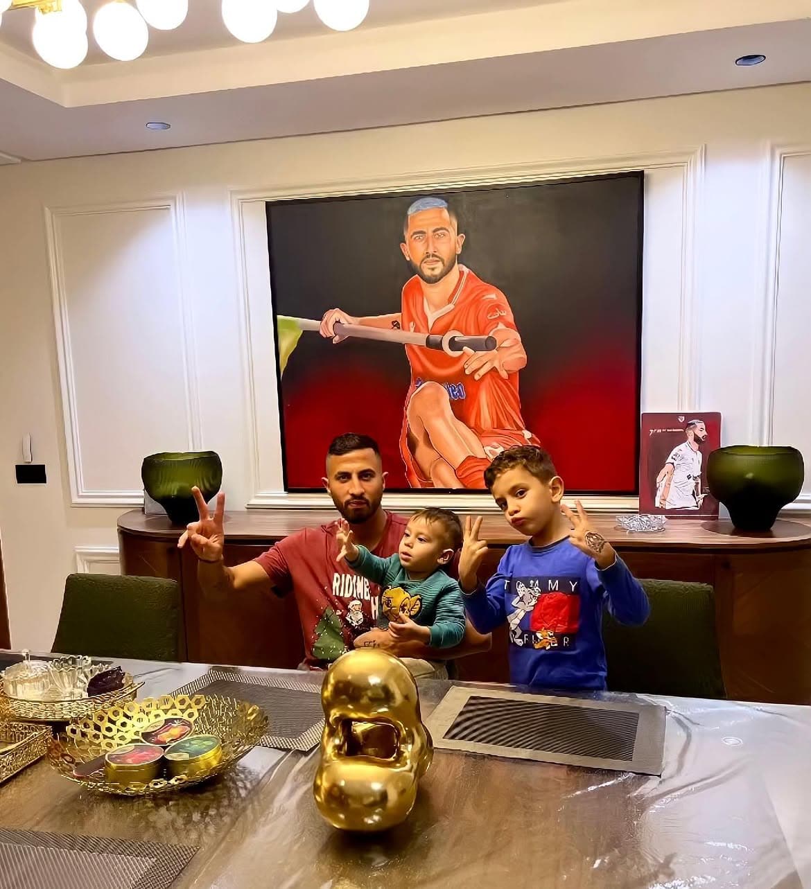 Kamal Hannouda with Aymane El Hassouni and his two young sons, posing in front of the framed portrait at home.