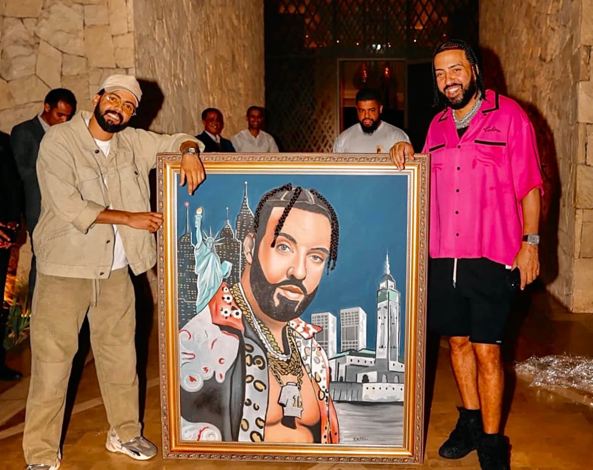 French Montana posing beside his framed portrait painting, which depicts him against a New York and Casablanca skyline.