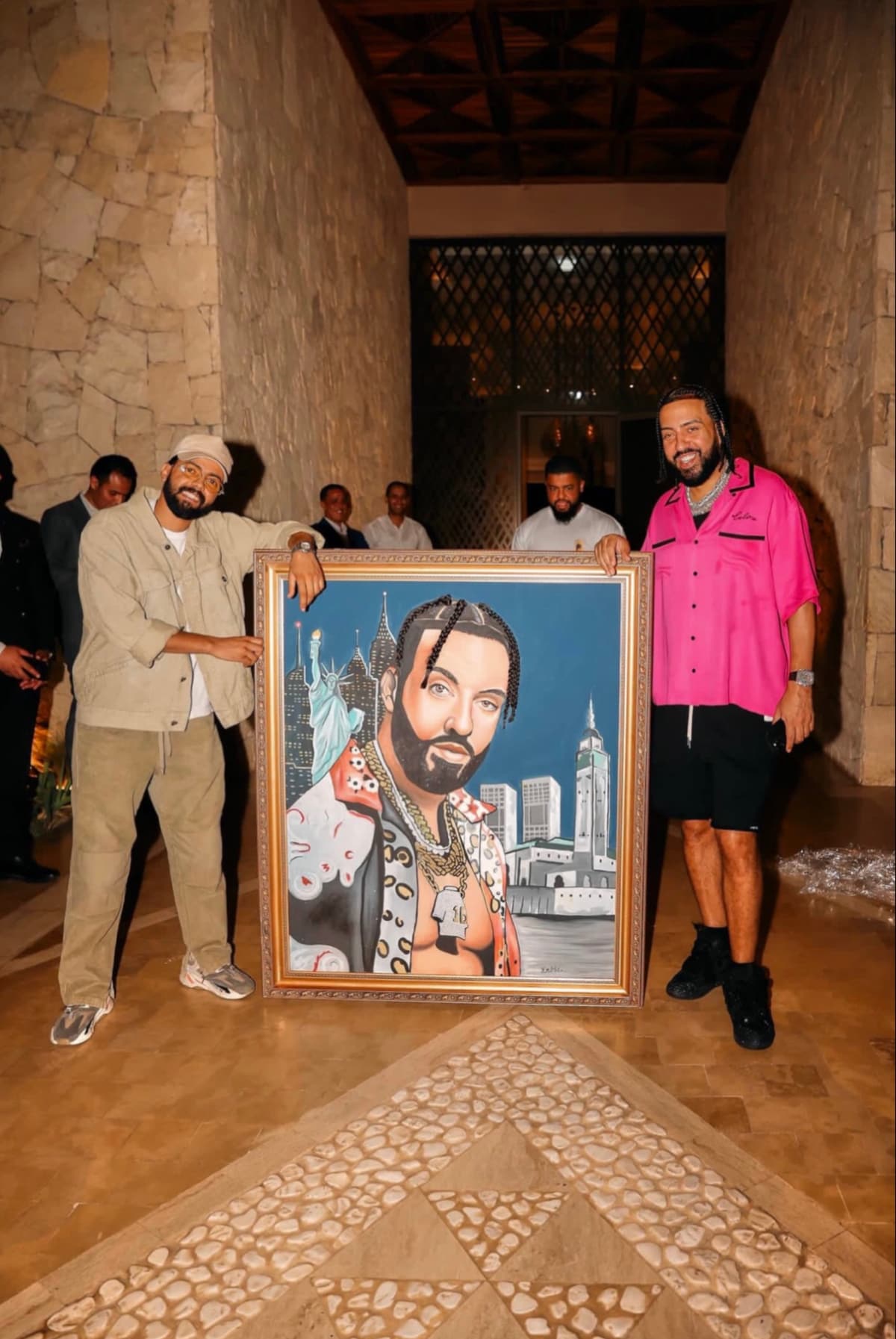 French Montana and Kamal Hannouda holding the framed portrait painting together in a stone hallway.