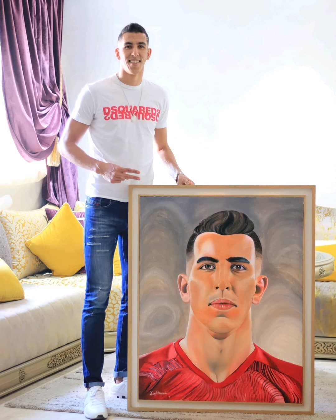 Framed portrait painting of Jawad El Yamiq in a Morocco national team jersey, held up by him for the camera.