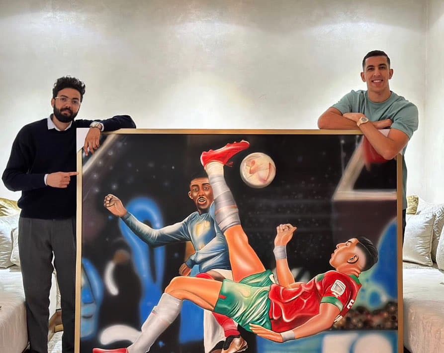 Two men holding a framed painting of a footballer performing an overhead bicycle kick.