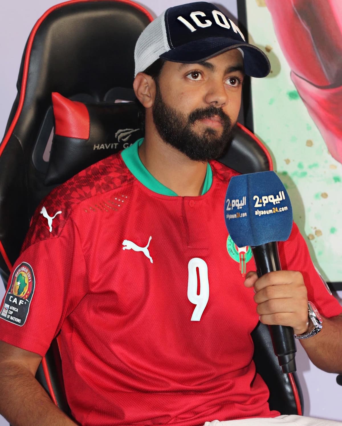 Kamal Hannouda seated in a gaming chair wearing a Morocco team jersey, being interviewed with a branded microphone.