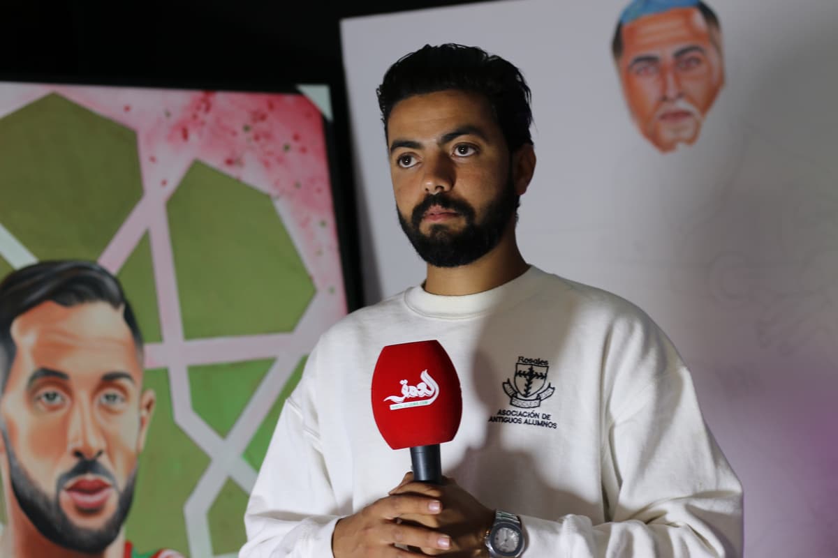 Kamal Hannouda being interviewed on camera in front of paintings, including a portrait sketch.