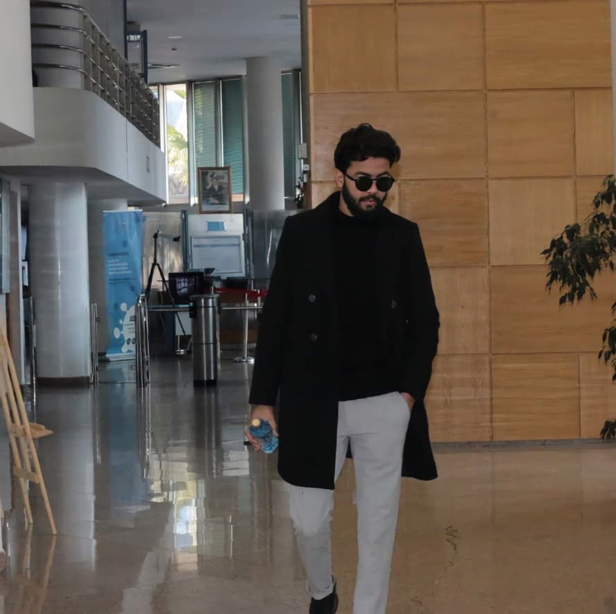 Kamal Hannouda walking through a marble lobby wearing a dark coat and sunglasses.