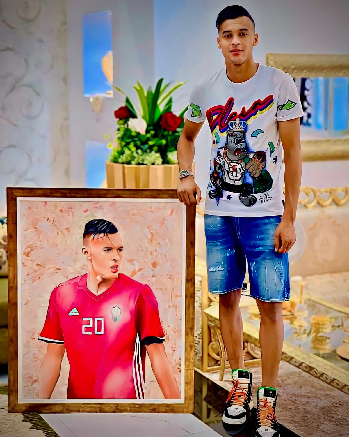 A footballer in an orange tracksuit standing beside his framed portrait painting.