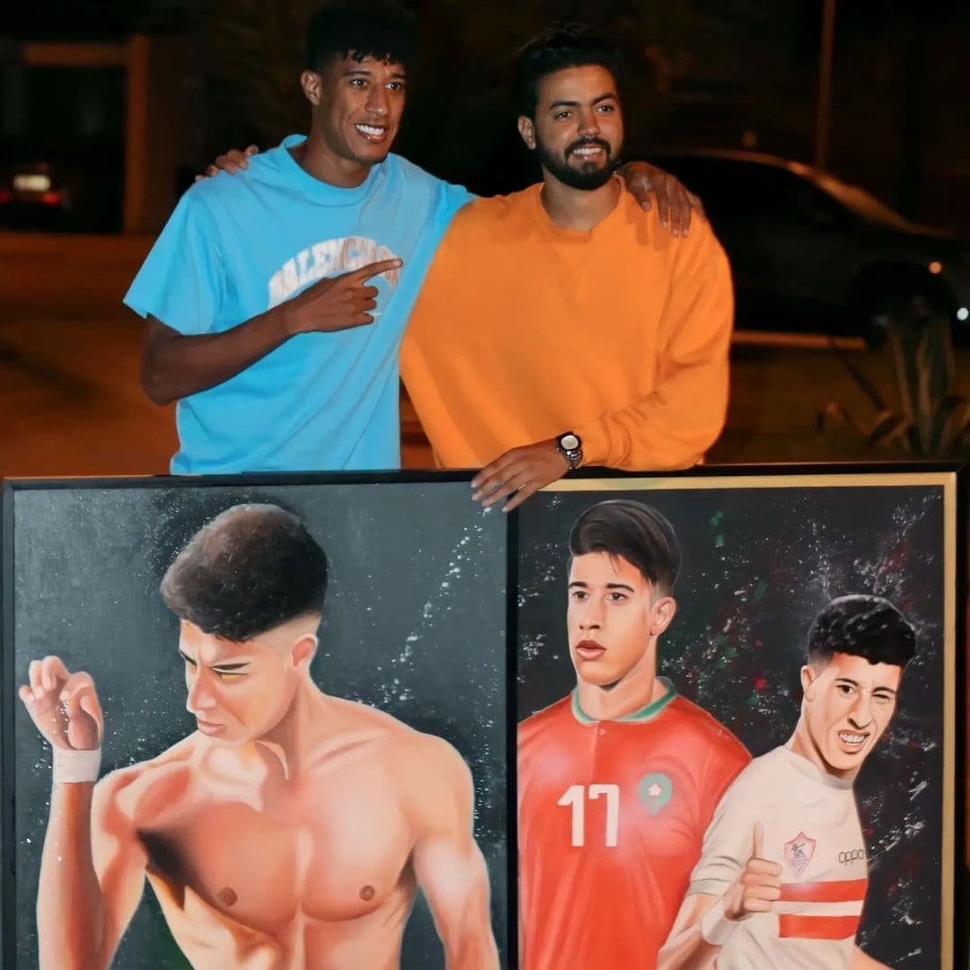 Two men holding a framed painting split between a shirtless boxing pose and a footballer in a Morocco jersey.