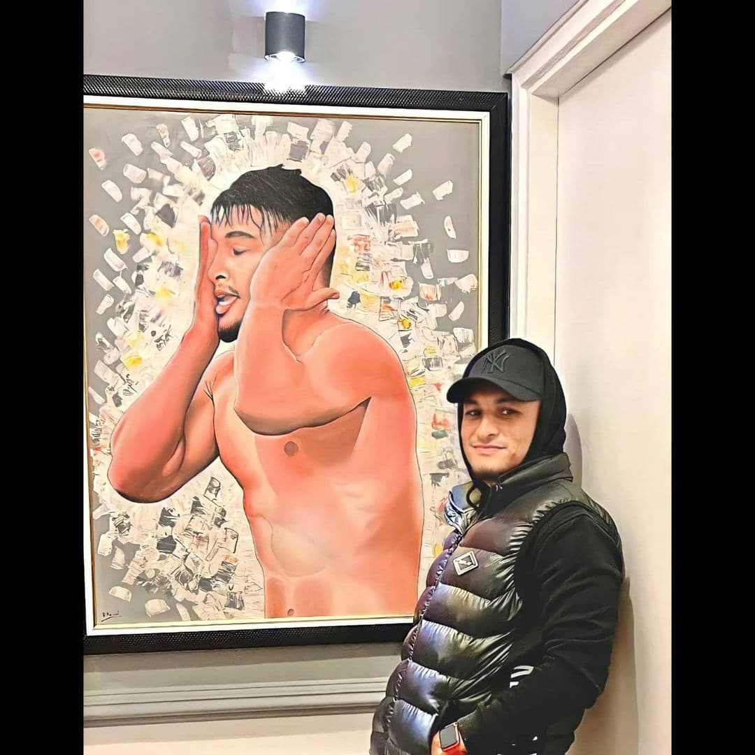 A framed painting of a footballer covering his face with both hands, displayed beside a man in a cap.
