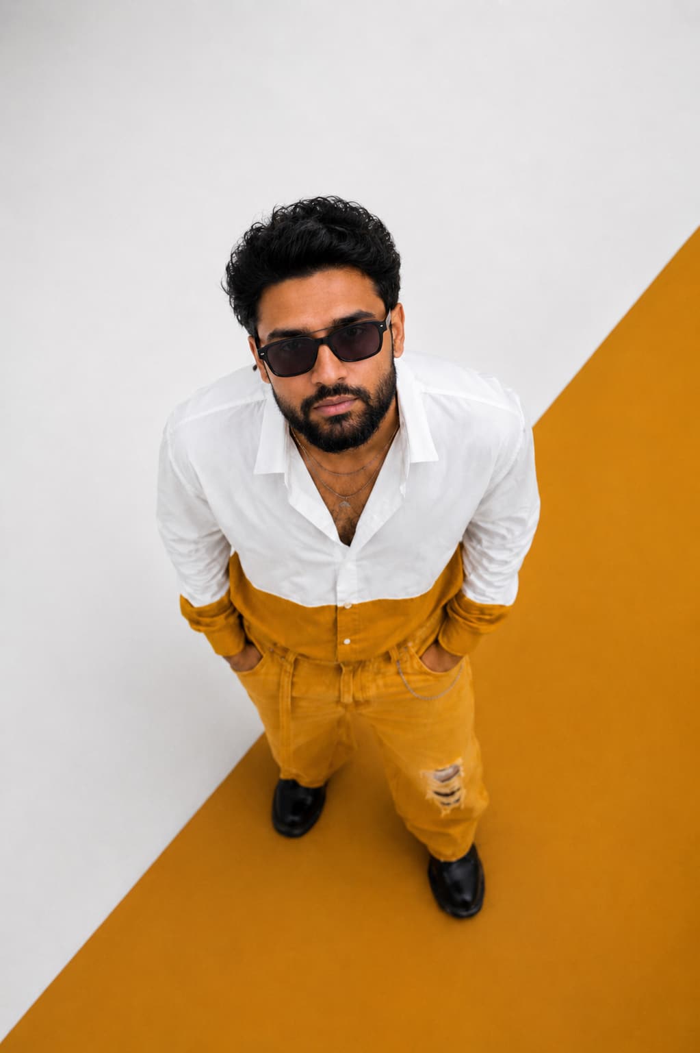 A man in a white-and-mustard color-blocked outfit standing on a matching color-blocked floor, echoing the ROOTED panels.